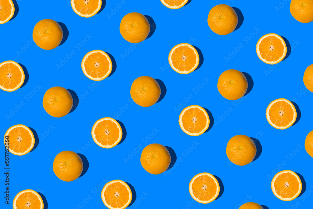 Summer flat lay pattern made with fresh whole orange fruit and slices on vibrant blue background. Minimal sunlight concept with sharp shadows