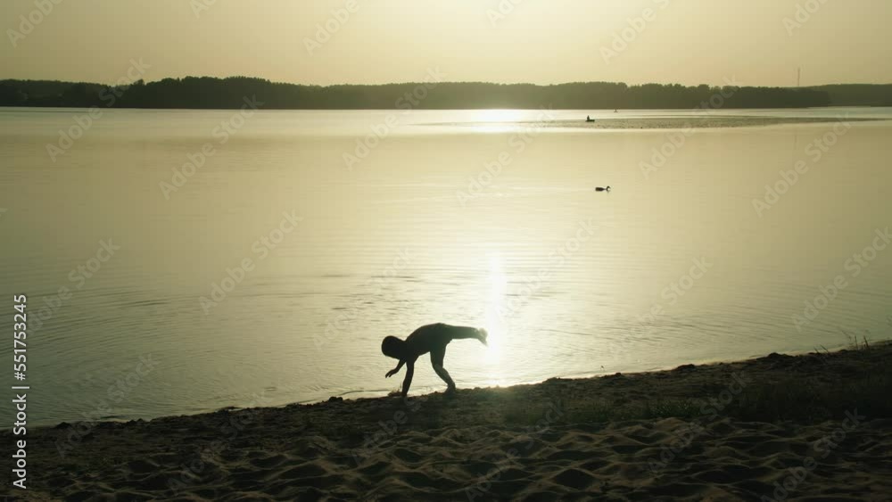 Silhouette of a carefree boy who jumps and runs across the sand right into the lake at sunset. Bathing and splashing with water. Healthy lifestyle Silhouette of a carefree boy who jumps and runs across the sand right into the lake at sunset. Bathing and splashing with water. Healthy lifestyle