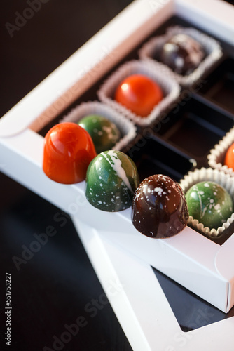 Set of different handmade chocolates in a white paper box on a black background. Holiday concept. Close up. Top view