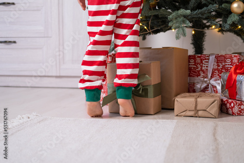 close up kid legs in Christmas pajamas near gift boxes and Christmas tree