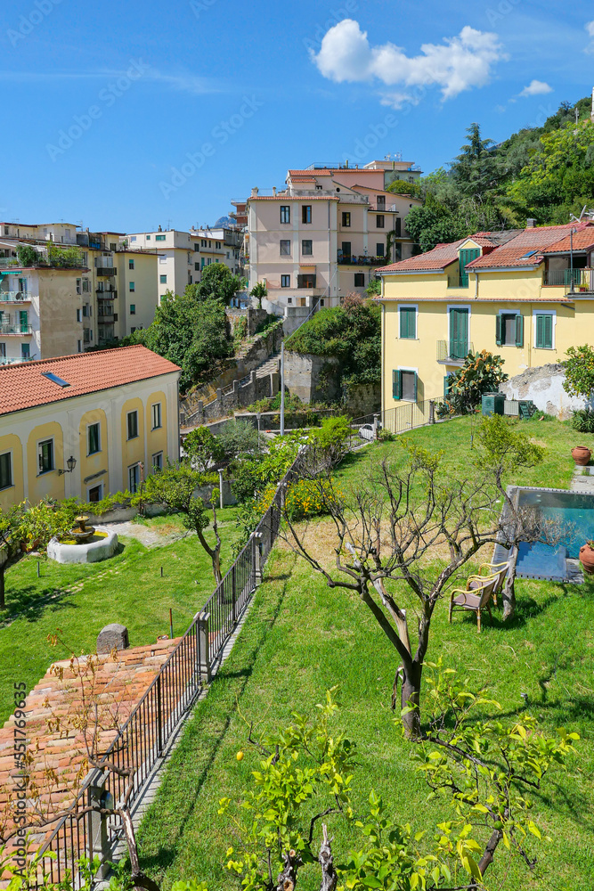 Italian houses in the greenery on the slope. You can see the trees, the pool, and the chairs beside it.