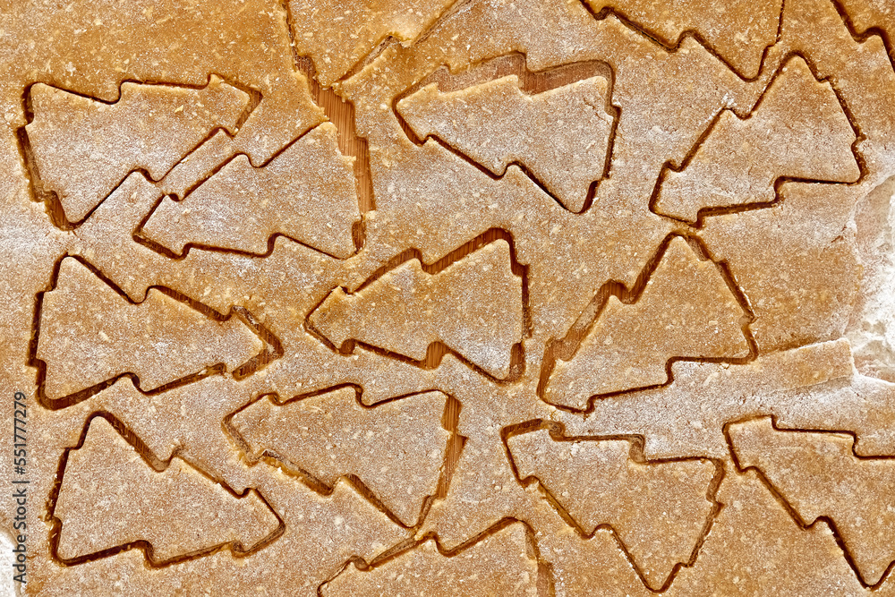 Flatted dough for christmas gingerbread cookies with cutted biscuits a shape of christmas tree. Baking homemade pastries from online recipe. Christmas and New Year traditions festive food.
