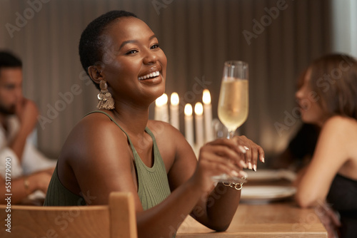 Champagne, celebration and happy black woman at a party or dinner at a table in the dining room. Happiness, smile and African lady enjoying a glass of alcohol beverage at a new year event at a house.
