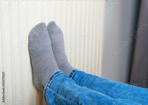 Warming Feet on White Radiator, Man Warms his Feet at Home, Cold Winter, Expensive Electricity Saving Concept