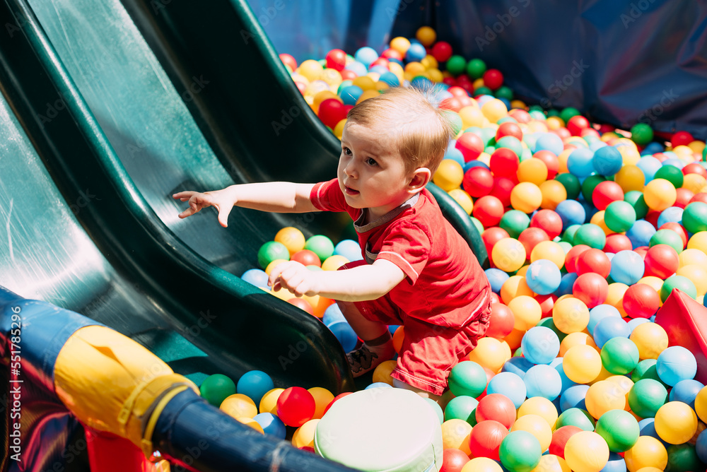 Obraz premium Happy laughing boy 1-2 years old having fun in ball pit in kids amusement park and indoor play center. Activity toys for little kid