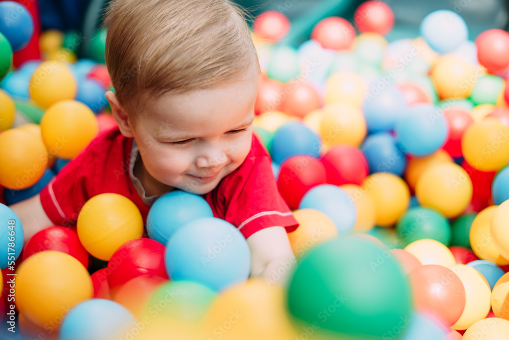 Obraz premium Happy laughing boy 1-2 years old having fun in ball pit in kids amusement park and indoor play center. Activity toys for little kid