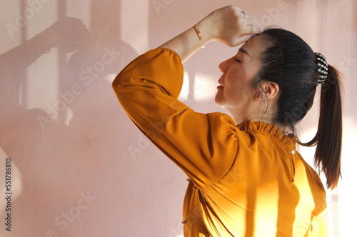 Woman wearing an orange outfit stands, tilts her head to the side, touches her own forehead with her hand, and listens to music, letting her emotions flow along with the sound of the music she hears. photo