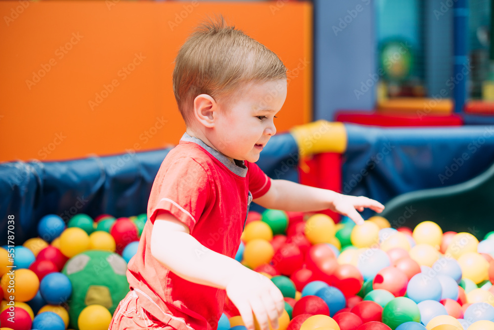 Obraz premium Happy laughing boy 1-2 years old having fun in ball pit in kids amusement park and indoor play center. Activity toys for little kid