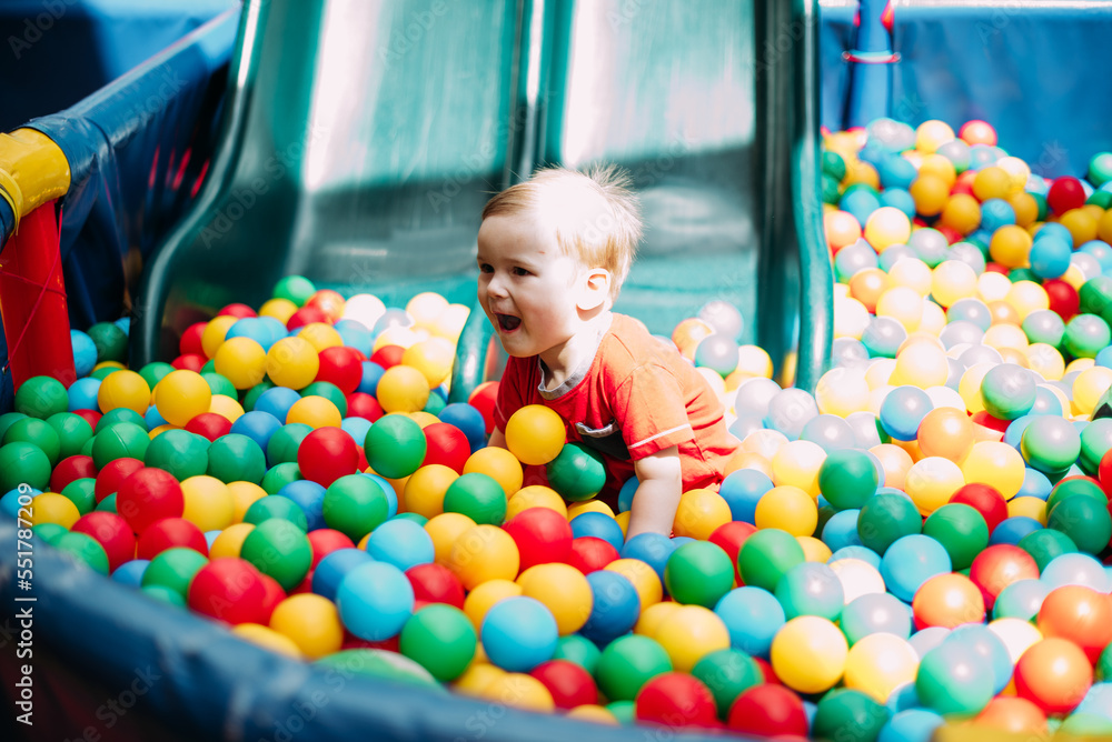 Obraz premium Happy laughing boy 1-2 years old having fun in ball pit in kids amusement park and indoor play center. Activity toys for little kid