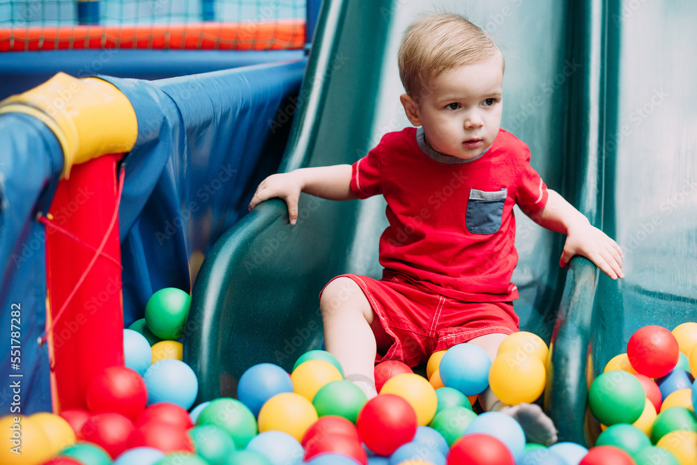 Obraz premium Happy laughing boy 1-2 years old having fun in ball pit in kids amusement park and indoor play center. Activity toys for little kid