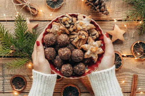 Flat lay photo of hands holding plate of christmas cookie over wooden boards with decorations