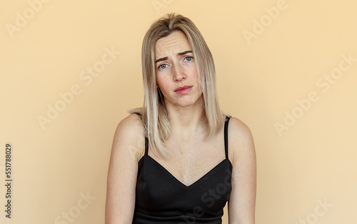 Sad and indifferent young woman with freckles, looking with boredom at camera, staring reluctant and upset, beige background