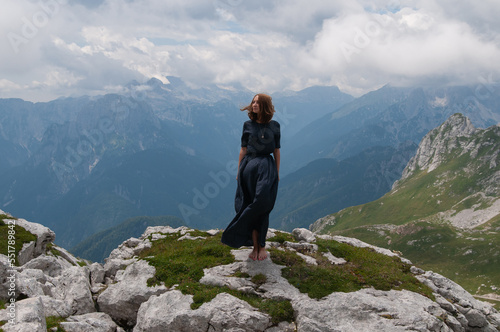 Beautiful young woman posing in a high mountain landscape. Rocky mountain. A young woman in a long dress stands on the edge of a cliff