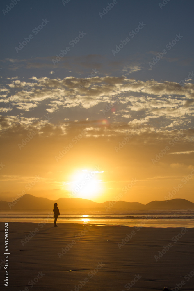 Incredible seascape. Sunset on the beach, clouds golden in the sun. the sun sets behind the mountains. silhouettes of mountains. The ocean washes the sand on the beach. Golden clouds. Background. Lanz