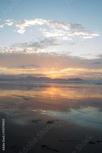 Incredible seascape. Sunset on the beach  clouds golden in the sun. the sun sets behind the mountains. silhouettes of mountains. The ocean washes the sand on the beach. Golden clouds. Background. Lanz