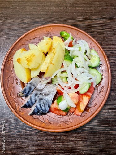 large vertical photo. homemade food. boiled potatoes with pieces of salted mackerel and vegetable salad on a brown clay plate. eco. bio.