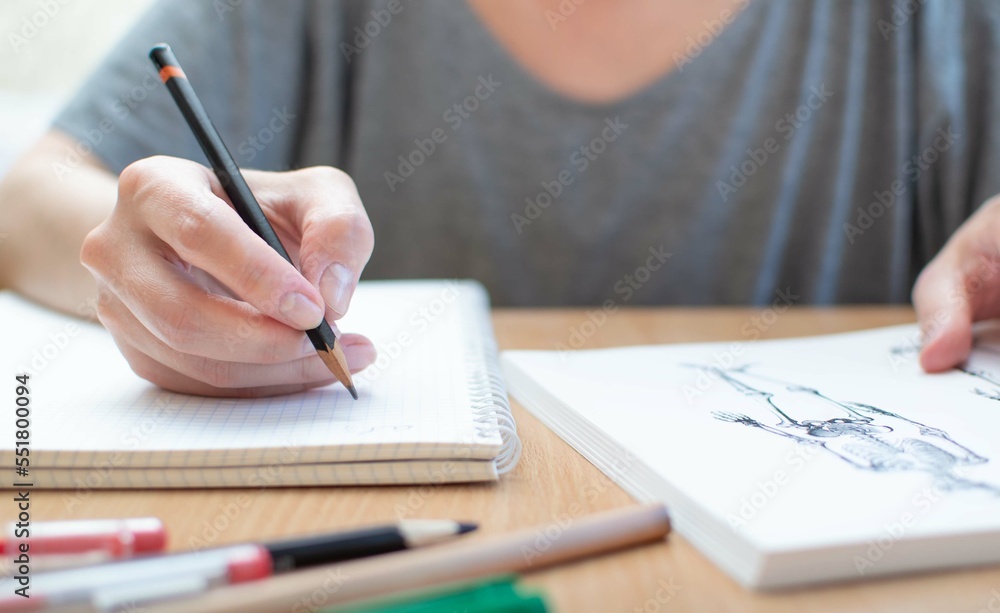 A woman sitting at a table looks at a textbook on anatomy and makes notes in a notebook. Educational concept. Selective focus. A woman sitting at a table looks at a textbook on anatomy and makes notes in a notebook. Educational concept. Selective focus.