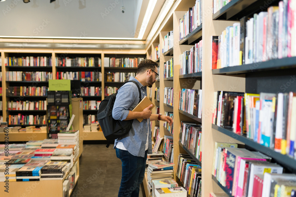 Caucasian man with a backpack browsing the bookshelves at the store Caucasian man with a backpack browsing the bookshelves at the store