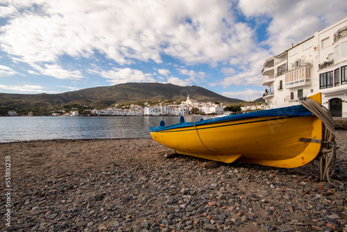 Barca amarilla y azul estacionada en una de las playas de piedra del pequeño pueblo de cadaqués en un día de otoño.