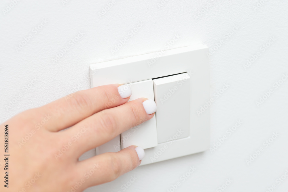 Turning on and off the light in the room with white walls. Close up picture of female hand on light switch Turning on and off the light in the room with white walls. Close up picture of female hand on light switch