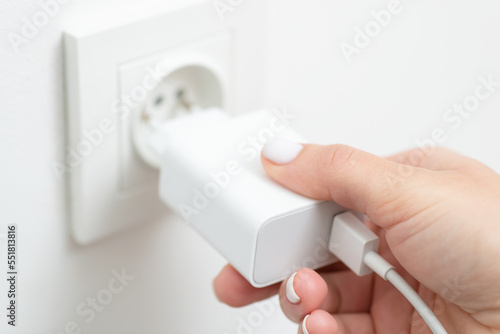 Female hand inserts charging device into electrical outlet, close up. Consumption of electricity, getting power to mobile phone to stay in touch with the world