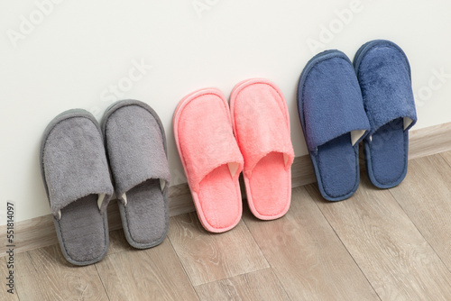 Three pairs of new home slippers stand on the grey floor near white wall. Cozy comfortable footwear for cold periods