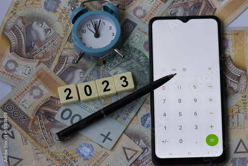 Concept for financial reminder to pay income tax in 2023. Polish money. Single hundred banknote on two hundred polish zloty background. Clock, pen and mobile phone calculator. Inscription PIT. photo