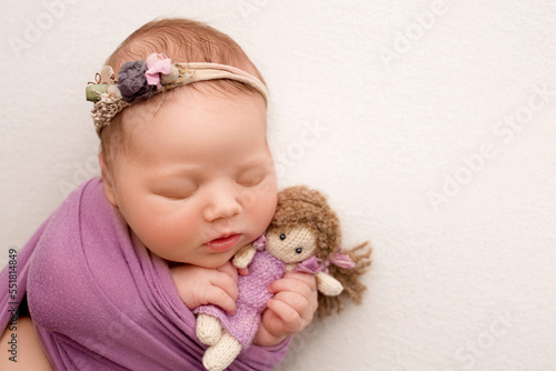 Sleeping newborn girl in the first days of life on a white background. A newborn baby in a purple lilac winding and a headband. Hand, palms of father and mother, parents hold the child.