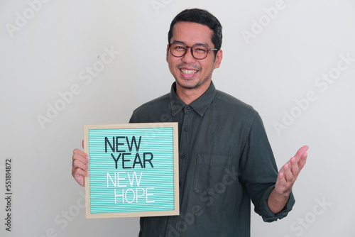 Adult Asian man holding wooden frame with New Year New Hope text photo