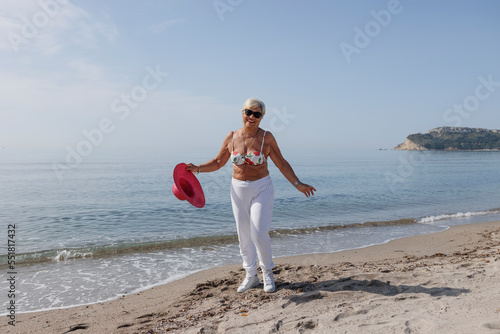 signora anziana con il cappello colore fucsia gioca in riva al mare in costume da bagno