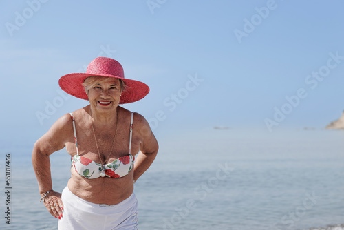 signora anziana con il cappello colore fucsia si gode il sole in riva al mare in costume da bagno