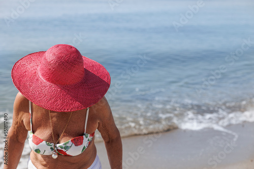 signora anziana con il cappello colore fucsia è fermaa in riva al mare in costume da bagno photo