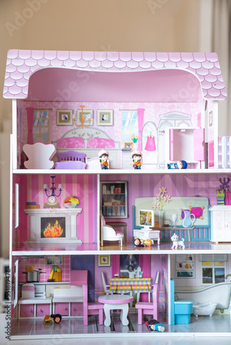 The photo of huge pink dollhouse model furnished with miniature furniture in a kid’s room.
