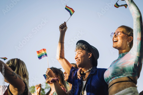 Happy man and woman with hands raised holding rainbow flags while enjoying in gay pride parade photo