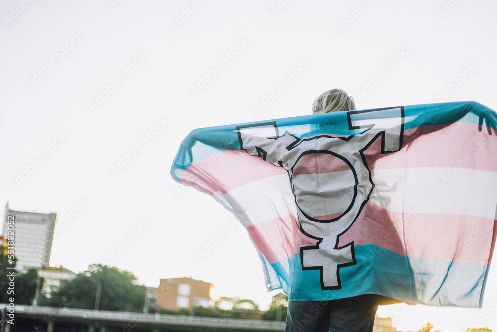 Rear view of non-binary person standing with LGBTQIA flag against clear sky Rear view of non-binary person standing with LGBTQIA flag against clear sky