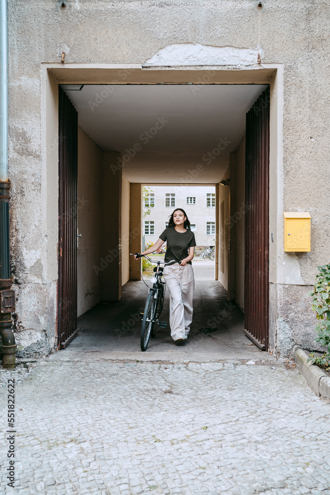Woman wheeling with bicycle while walking out of archival doorway Woman wheeling with bicycle while walking out of archival doorway