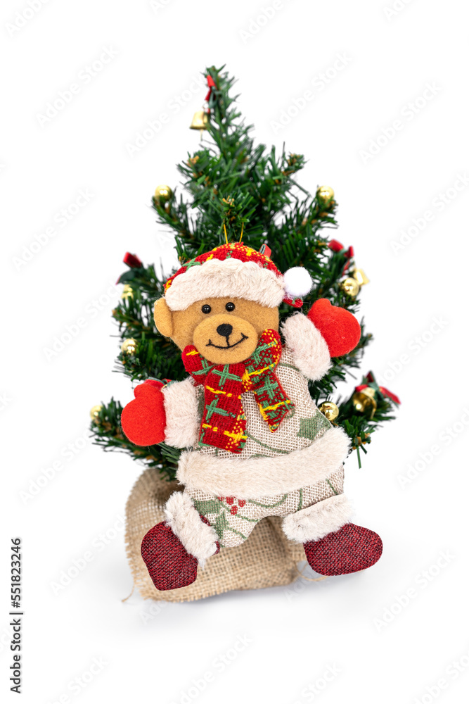 Teddy bear in Santa Claus costume hanging ornaments on the small Christmas tree isolated on white background.