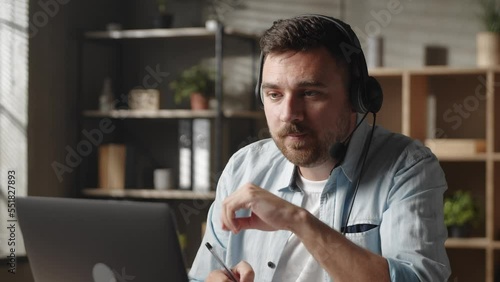 Concentrated young male worker employee entrepreneur in headphones, holding negotiations meeting online with client or colleagues, using computer video call app