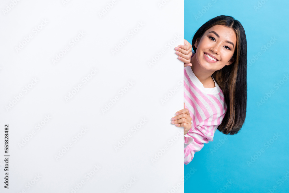 Photo of smiling attractive japanese woman black hair hide behind big paper poster promoter mockup new brand sale isolated on blue color background Photo of smiling attractive japanese woman black hair hide behind big paper poster promoter mockup new brand sale isolated on blue color background