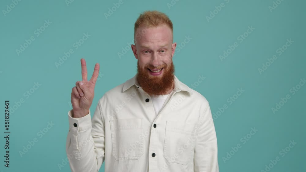 Caucasian, red-haired man looking cheerful and happy while showing a V sign. Portrait of a smiling guy making a gesture for victory. High quality 4k footage Caucasian, red-haired man looking cheerful and happy while showing a V sign. Portrait of a smiling guy making a gesture for victory. High quality 4k footage