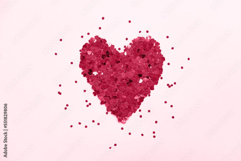 Heart made of shiny red small decorative hearts on a pink background strewn with sparkles. Flat lay, place for text. 