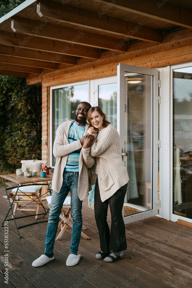 Portrait of happy multiracial couple standing on porch outside house Portrait of happy multiracial couple standing on porch outside house