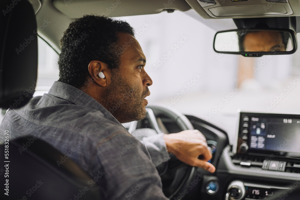 Male professional wearing wireless inear headphones driving car Stock