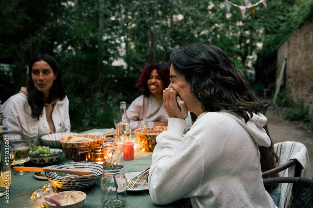 Side view of woman laughing while sitting at dining table during dinner party Side view of woman laughing while sitting at dining table during dinner party
