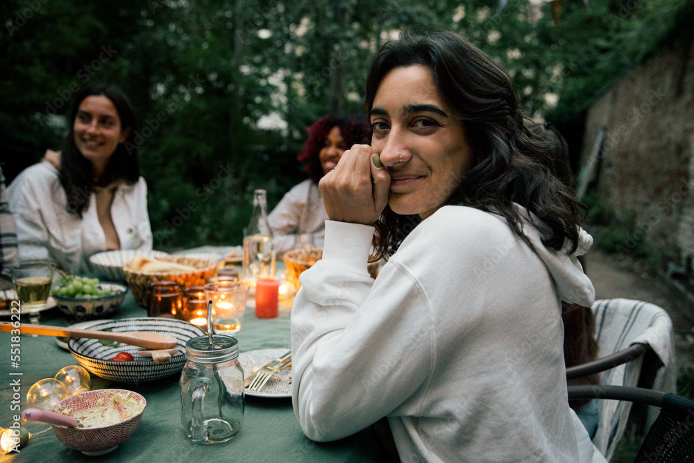 Portrait of smiling woman at dining table during dinner party in back yard Portrait of smiling woman at dining table during dinner party in back yard