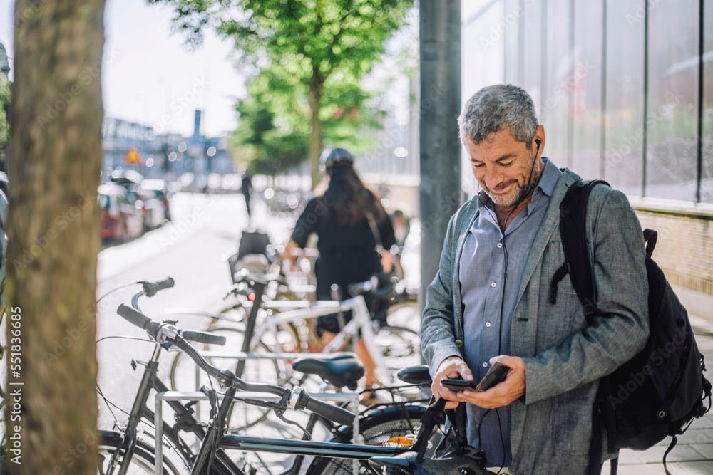 Smiling mature businessman using smart phone while standing at bicycle parking station Smiling mature businessman using smart phone while standing at bicycle parking station