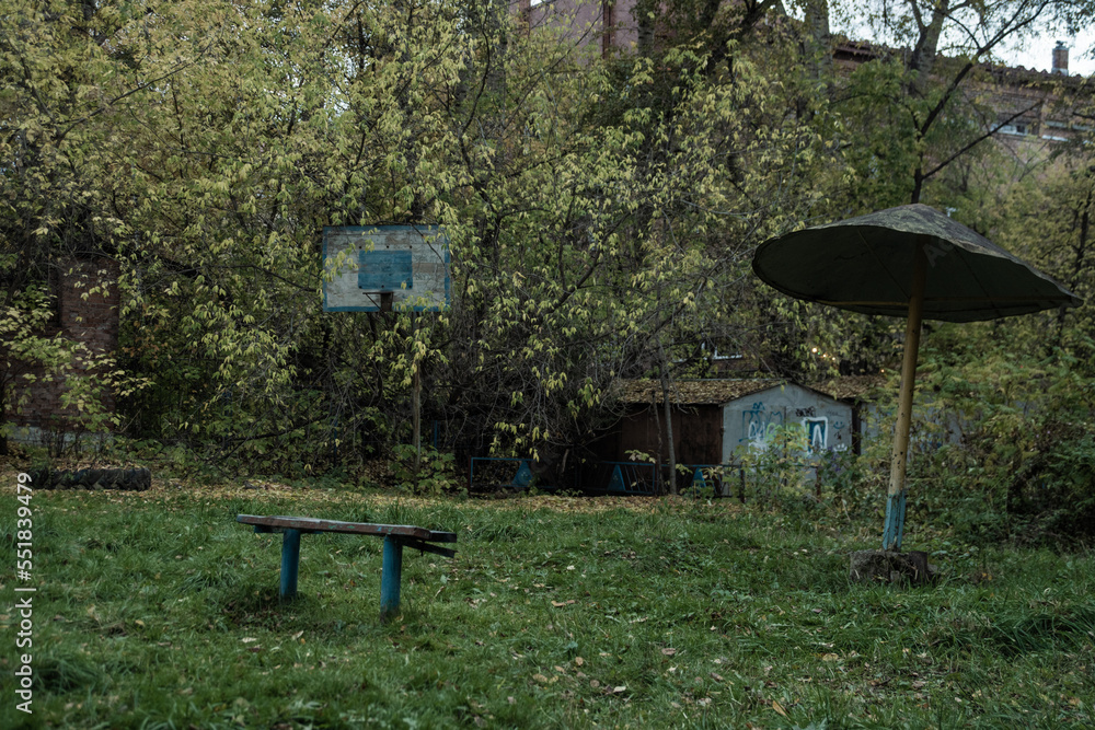 Soviet playground in with rusted basketball hoop, shed, and wooden park bench Soviet playground in with rusted basketball hoop, shed, and wooden park bench
