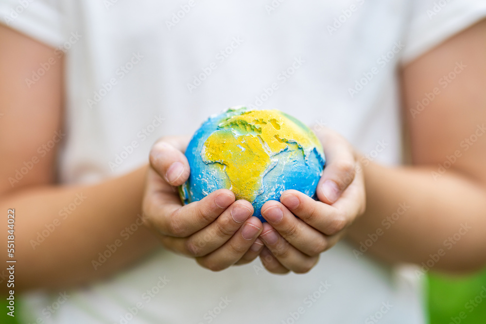 Kid holding small planet in hands against spring or summer green background. Ecology, environment and Earth day concept. Kid holding small planet in hands against spring or summer green background. Ecology, environment and Earth day concept.