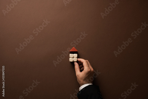 Hand of a businessman building a house of simple plain wooden blocks