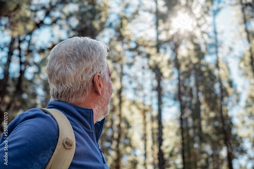 Senior white-haired man in mountain excursion looking at the sky - elderly handsome male enjoying retirement and healthy lifestyle in outdoors
